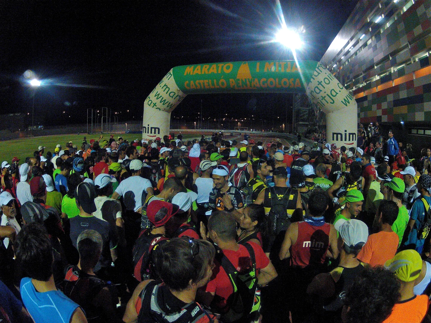Multitud de corredores bajo el arco de salida de la Marató i Mitja en un estadio iluminado