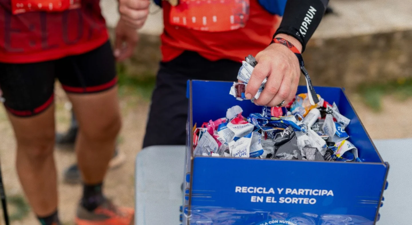 Mano depositando un envoltorio en una caja azul de recogida de residuos