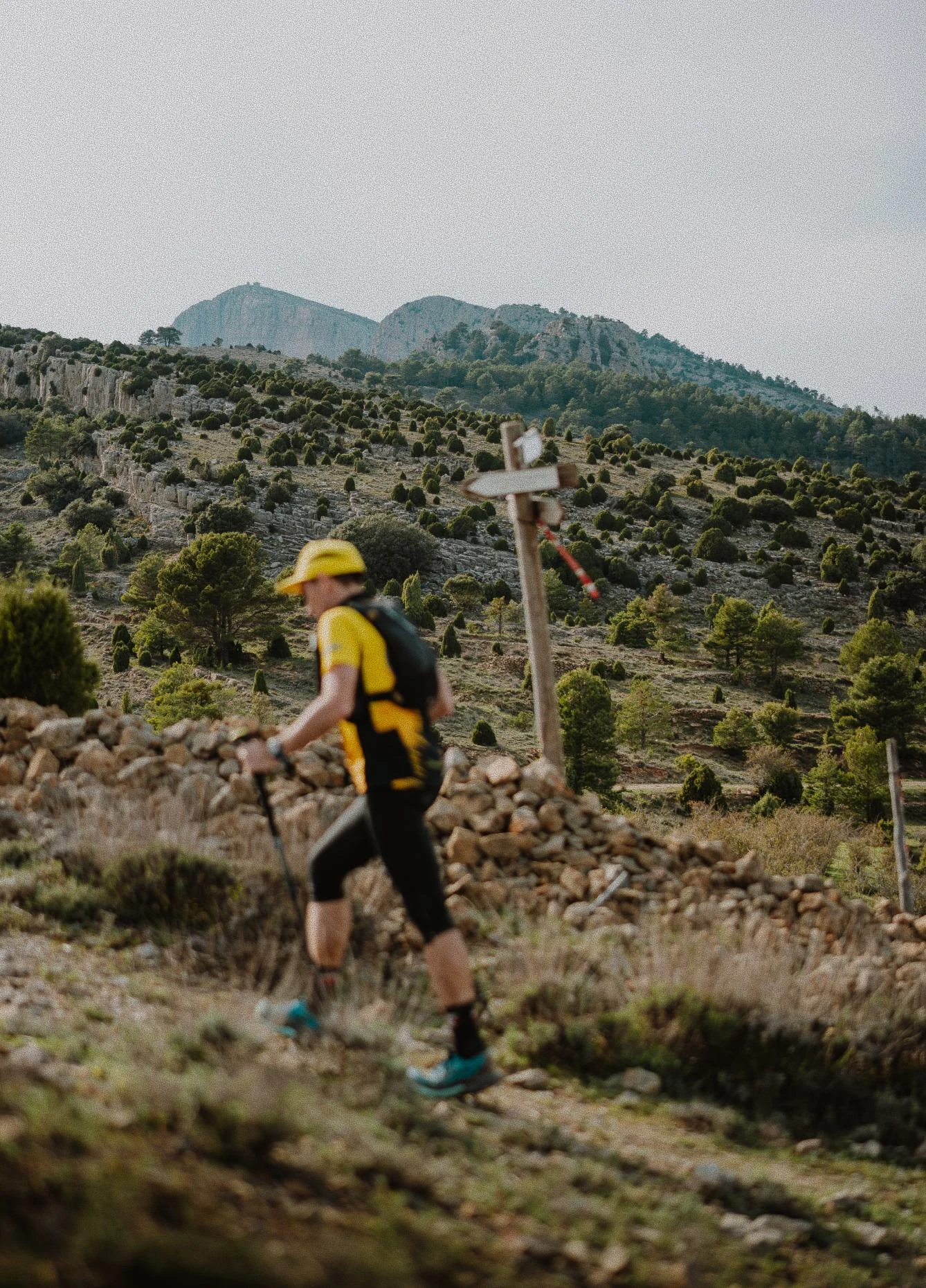 Participante con mochila amarilla junto a un muro de piedra en la montaña