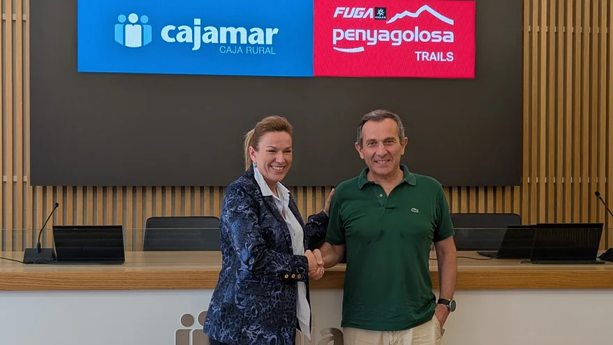 Una mujer y un hombre estrechan la mano bajo una pantalla con los logotipos de Cajamar y FUGA Penyagolosa Trails